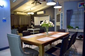 Un salón de conferencias con una mesa de madera, sillas negras y un jarrón de flores blancas.