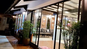 Un intérieur moderne avec une porte vitrée donnant sur un espace salon agrémenté d’un mur en briques et d’un plafond avec des poutres apparentes.