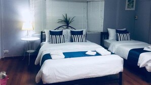 Une chambre d’hôtel avec deux lits, une petite table, une lampe et une fenêtre avec des stores.