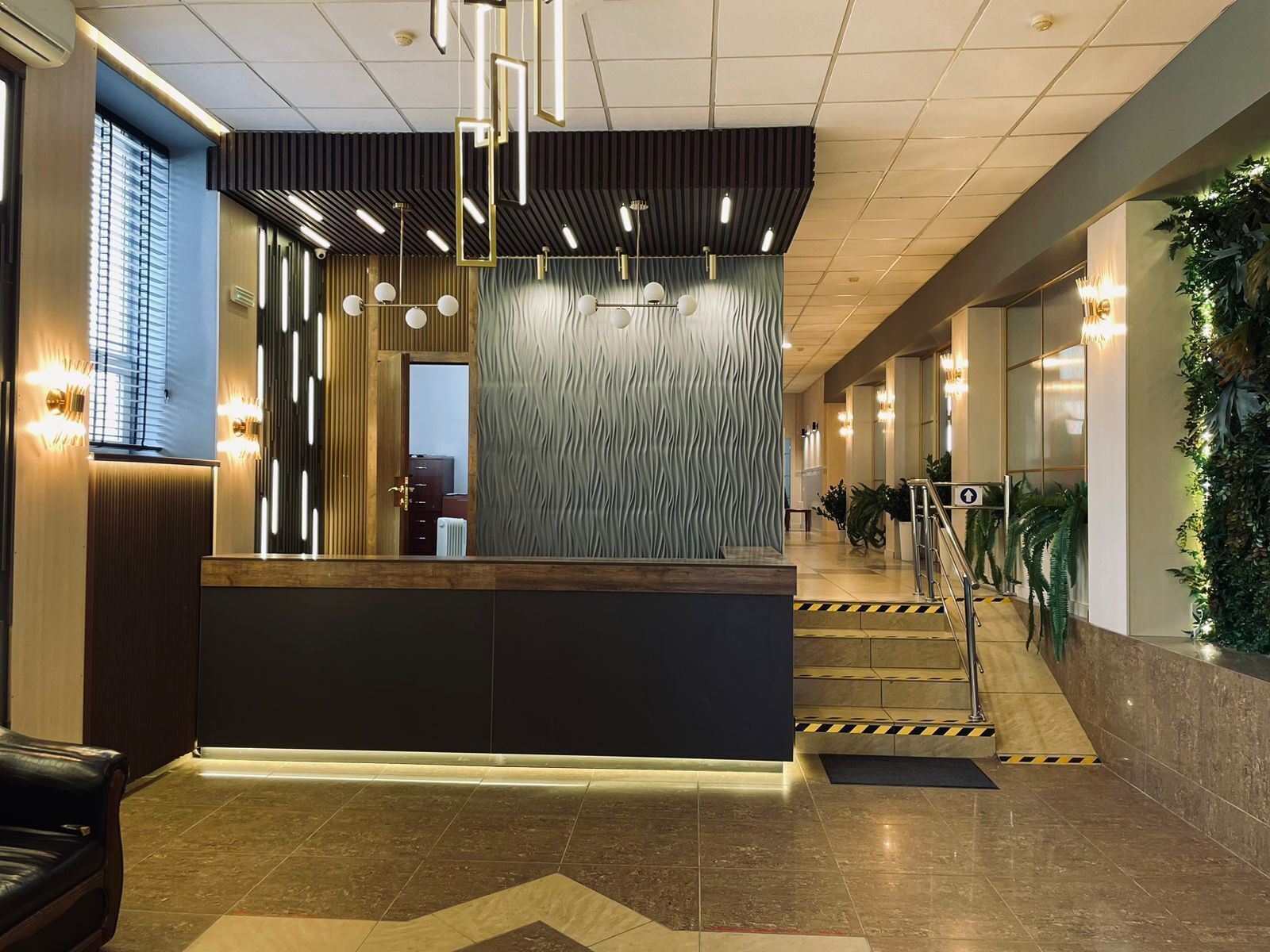 Ett välkomnande område med modern design, med en receptionsdisk, en vägg med ett intressant mönster och en trappa som leder upp till en övre våning.
