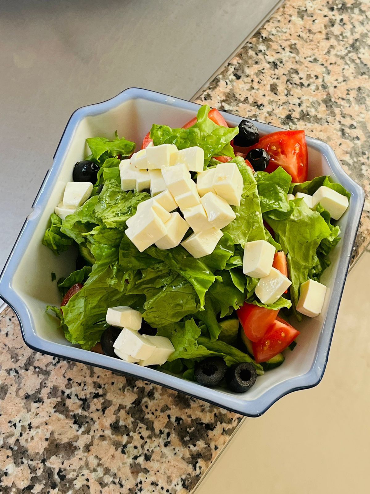 Uma saladeira com alface, tomates, azeitonas pretas e cubos de queijo.