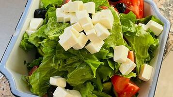 Uma saladeira com alface, tomates, azeitonas pretas e cubos de queijo.