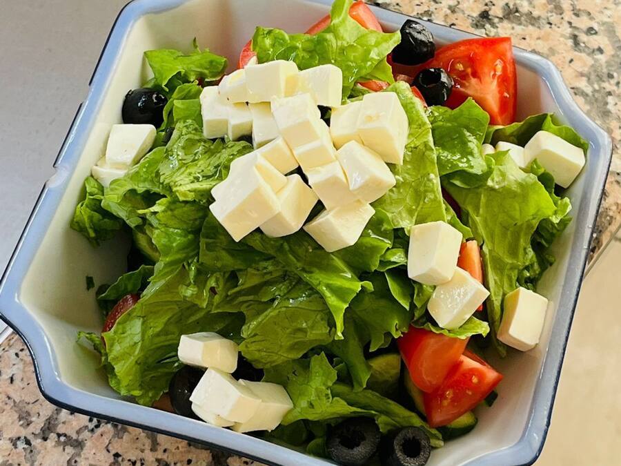 Uma saladeira com alface, tomates, azeitonas pretas e cubos de queijo.
