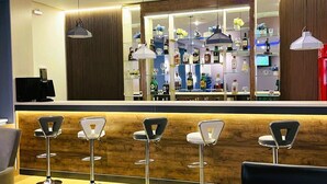 Eine Bar mit einer Holztheke, Barhocker und einer Auswahl an Flaschen und Gläsern.
