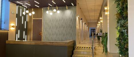 A modern hotel reception area with a reception desk, a staircase, and a wall with vertical wooden slats.