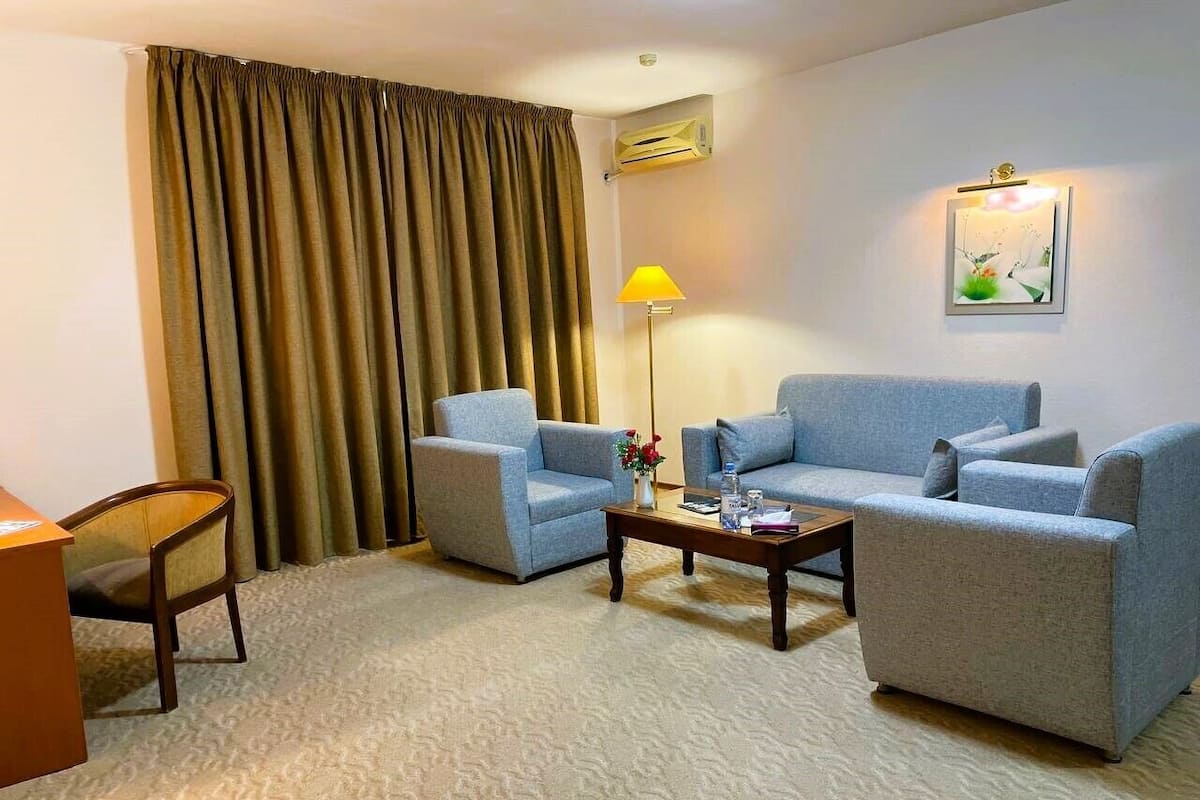 A hotel room with two grey sofas, a wooden coffee table, a desk, a chair, a lamp, and an air conditioning unit.