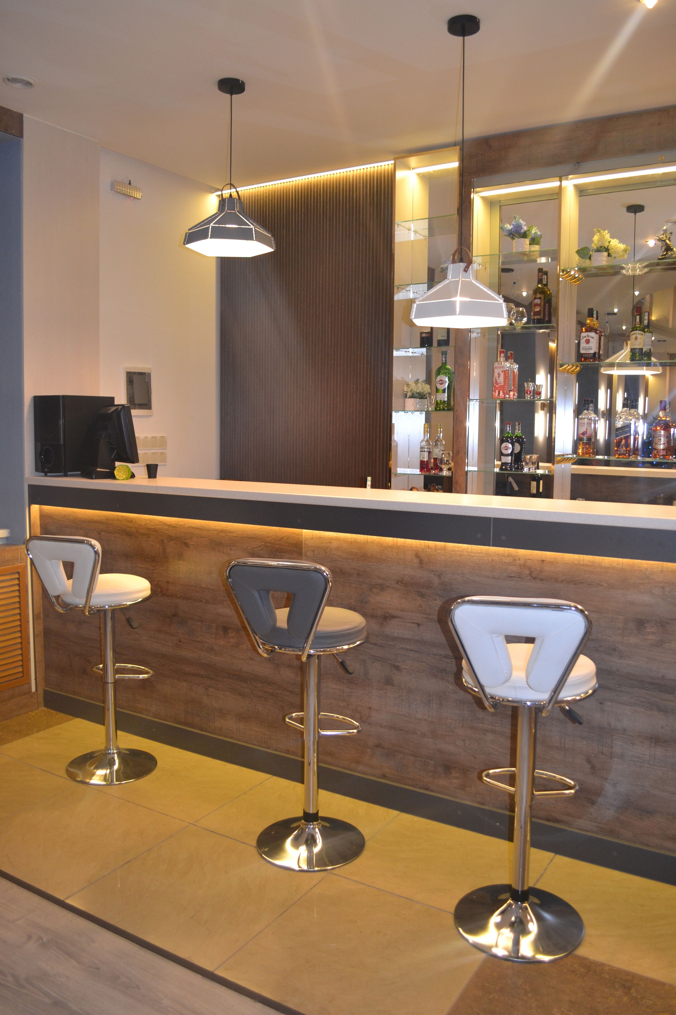 A bar area with three bar stools, a counter with a mirror, and overhead pendant lighting.