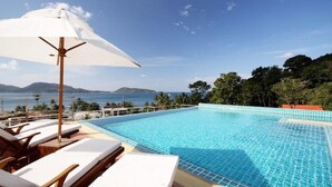 Uma piscina com água azul cristalina, rodeada por espreguiçadeiras e um guarda-sol, com vista para a paisagem da costa e colinas.