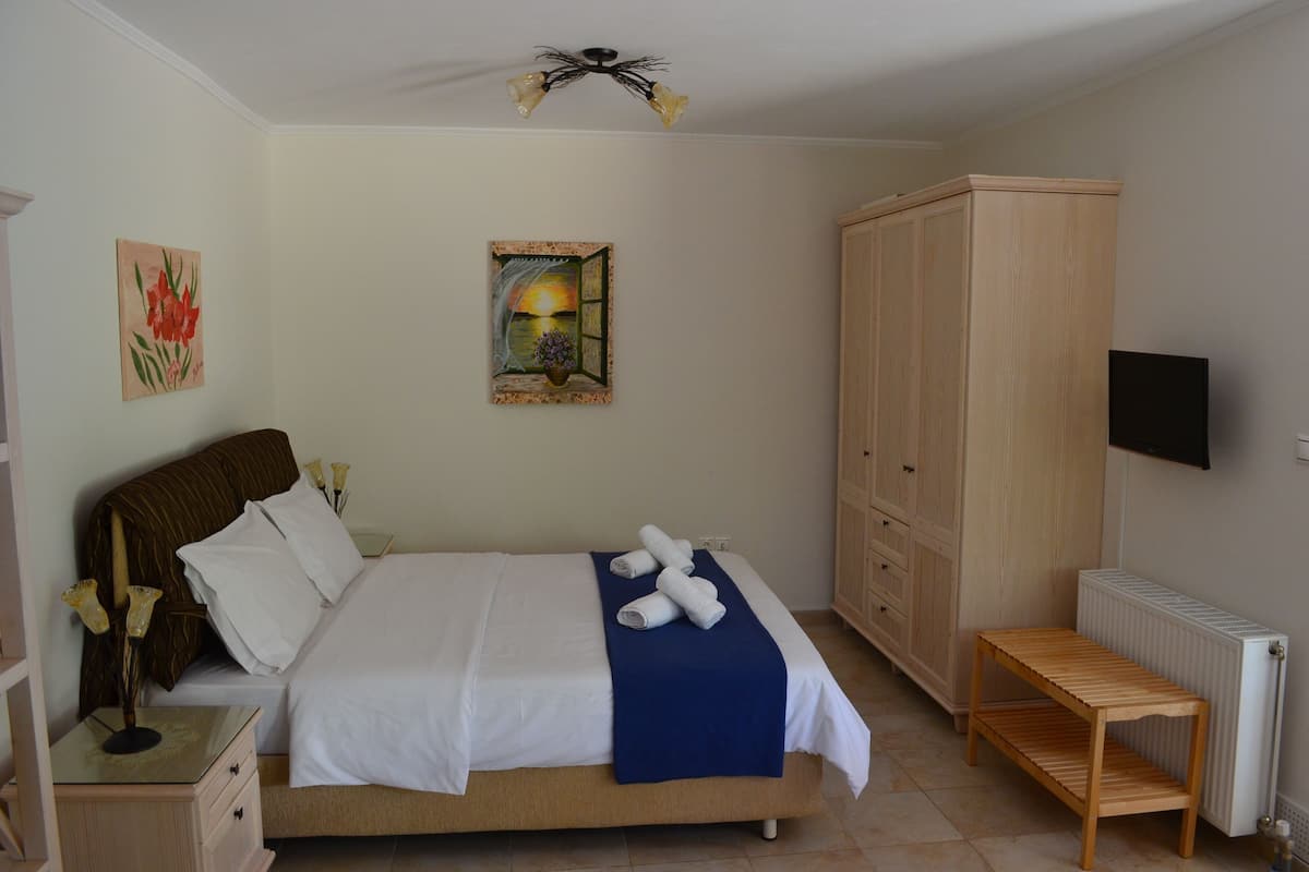Ein Schlafzimmer mit Bett, Nachttisch, Lampe, Kunstwerk, Kleiderschrank und Fernseher.