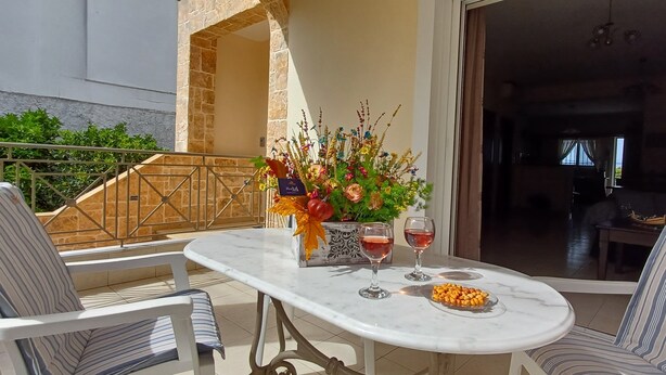 A patio with a marble table, two striped chairs, a vase with flowers, and two glasses of red wine.