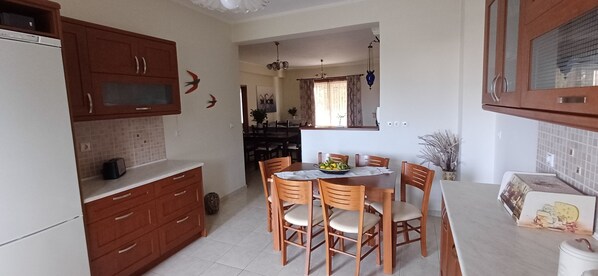 A compact kitchen with wooden cabinets, a dining table with chairs, and a refrigerator. - Blue Ark Aigeira Flat & Studio (Aigialeia)