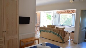 A bedroom with a bed, a TV mounted on the wall, a window with curtains, and a wooden door.