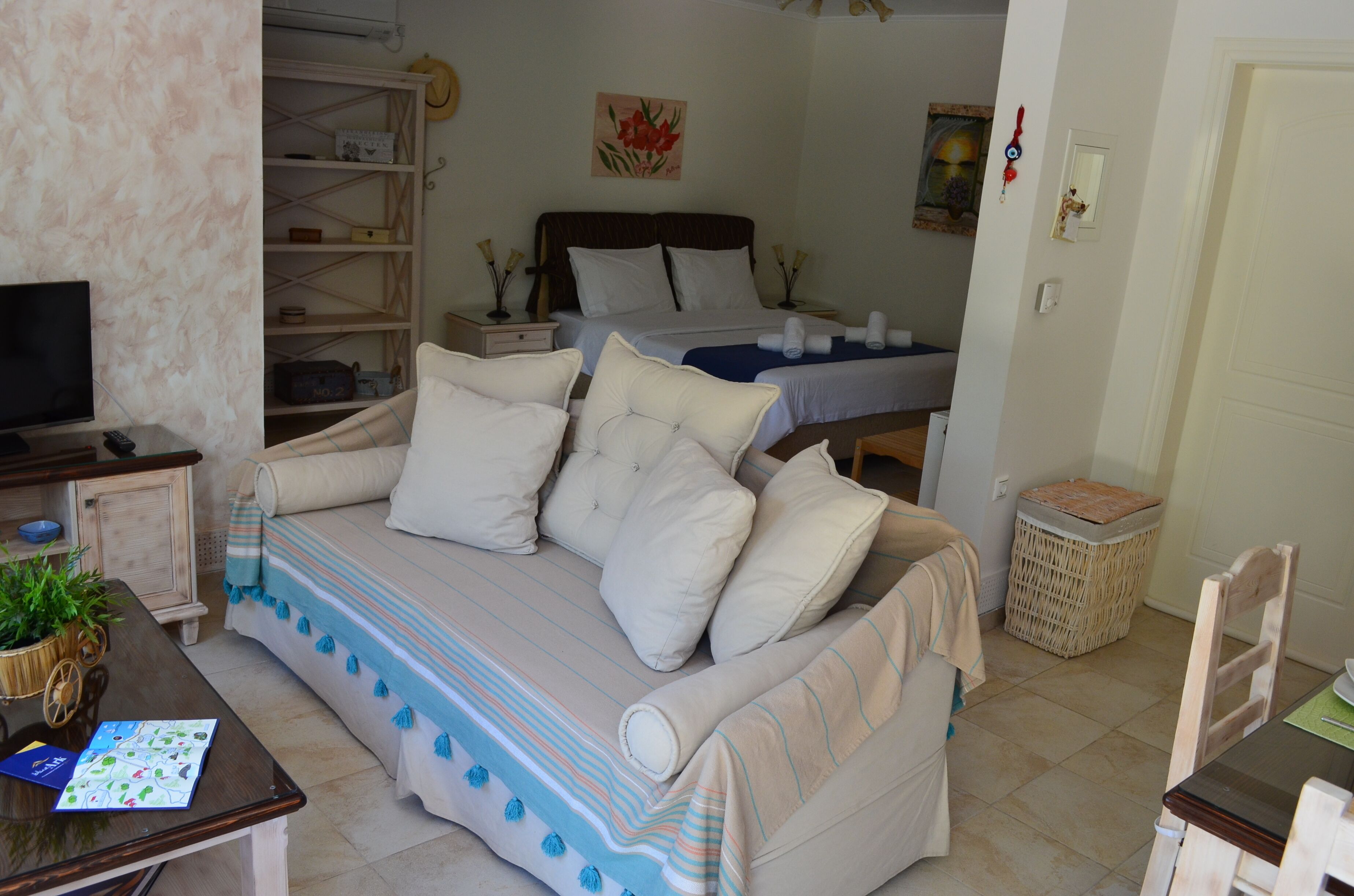 Una habitación acogedora con sofá, televisión, estantería y cama con cabecero.