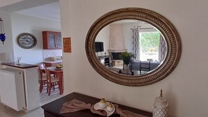 A dining area with a wooden table and chairs, a kitchen in the background, and a large mirror on the wall.