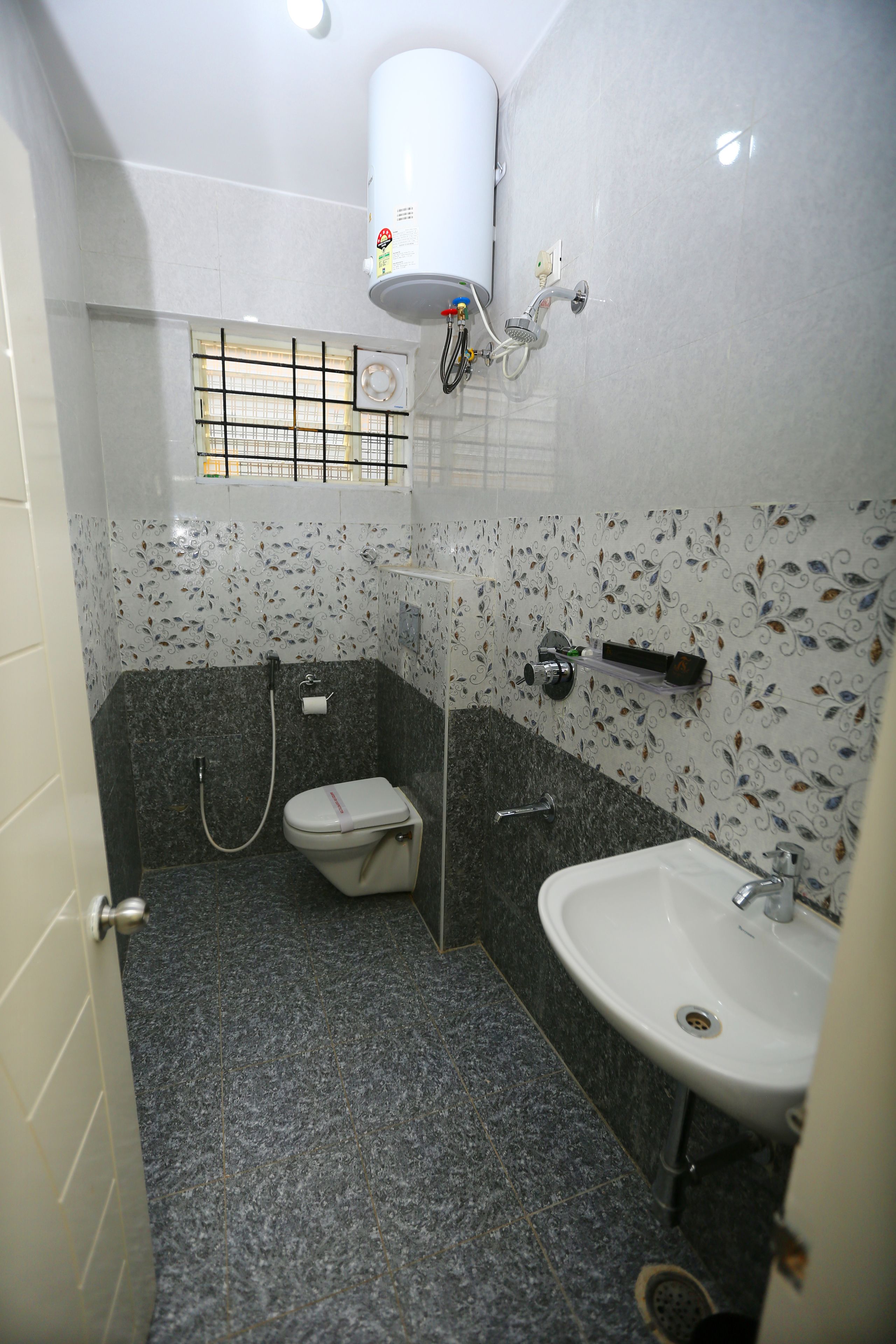 Ein Badezimmer mit Toilette, Waschbecken, Dusche und einem an der Wand montierten Boiler.