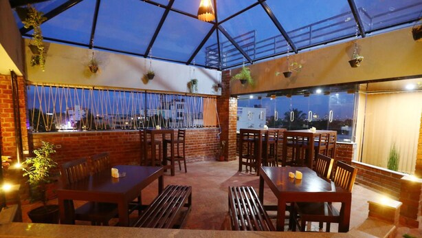 An outdoor dining area with brick walls, wooden tables and benches, hanging plants, and a glass ceiling. - Hotel The Shack (Bengaluru)