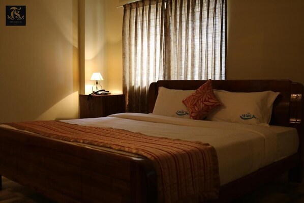 A hotel room with a wooden bed, a nightstand with a lamp, and a window with curtains.