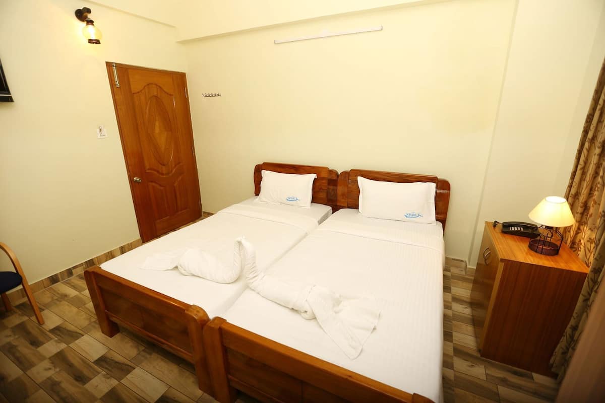 Una cama doble con ropa de cama blanca, un cabecero de madera, una mesita de noche con lámpara y una puerta de madera.