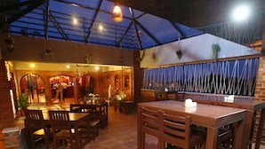 An indoor dining area with brick walls, wooden tables and chairs, hanging plants, and a glass ceiling. - Hotel The Shack (Bengaluru)