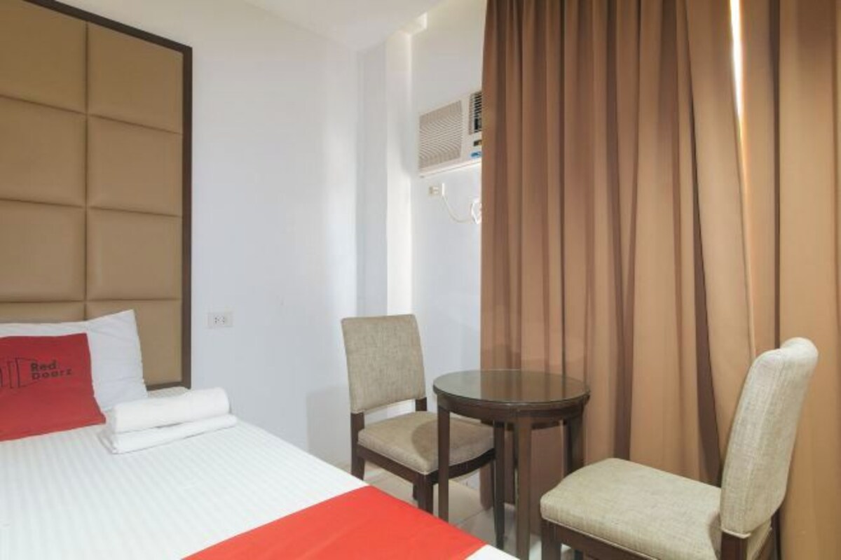 Een hotelkamer met een bed, twee stoelen, een tafeltje en een raam met gordijnen.