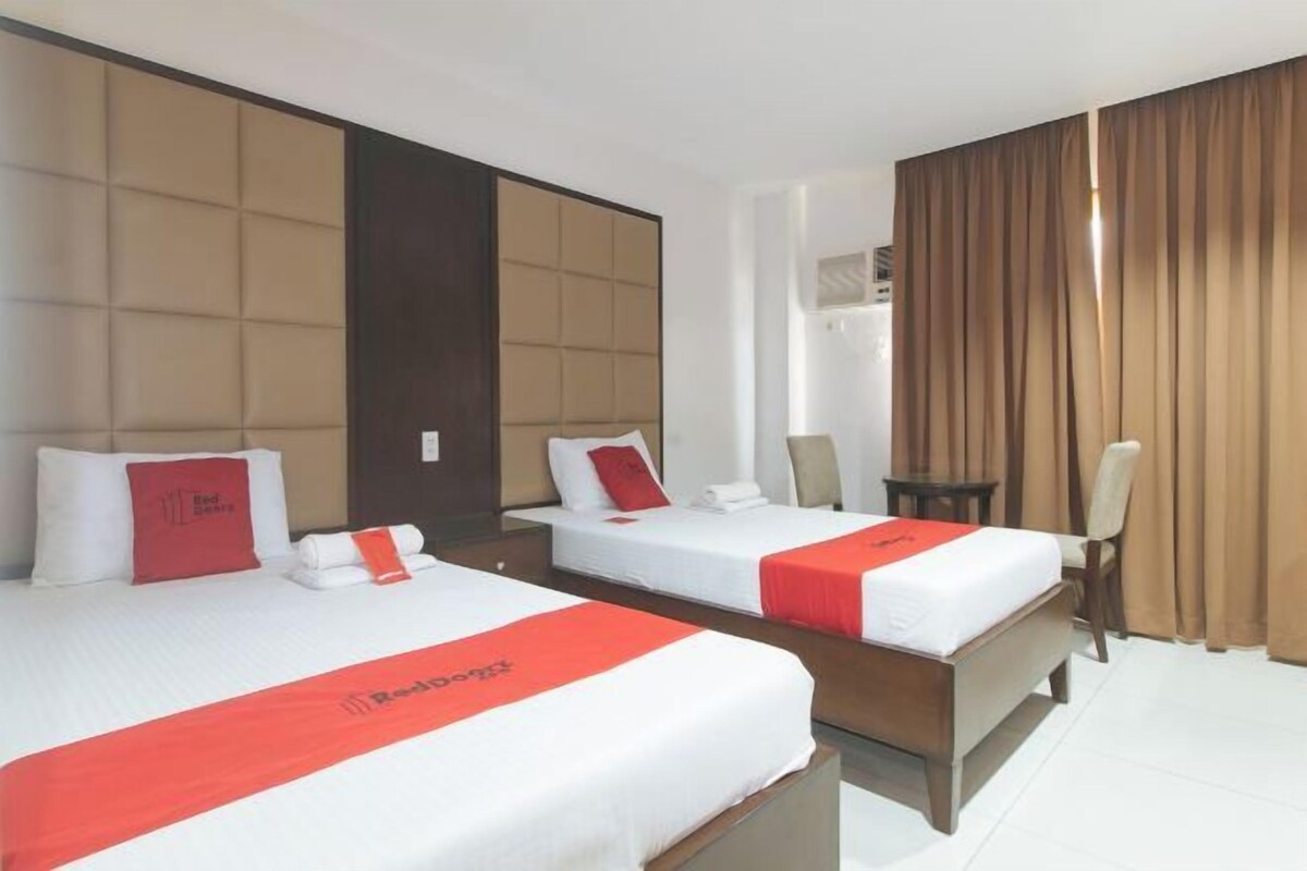 Une chambre d’hôtel avec deux lits, chacun recouvert d’une courtepointe rouge et blanche, doté d’une tête de lit et d’une petite table de chevet.