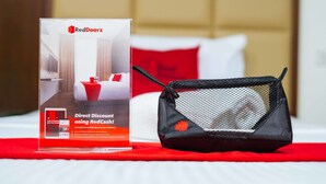 Une présentation promotionnelle pour RedDoorz comprenant une offre de réduction immédiate, un sac en filet noir et un couvre-lit rouge et blanc.