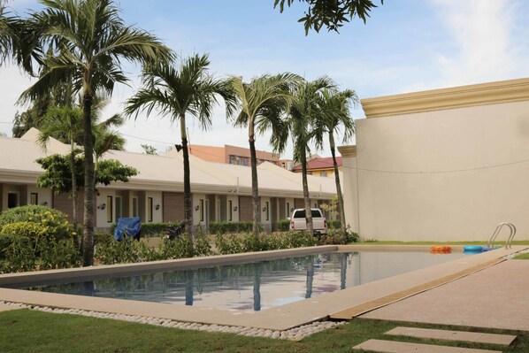 A swimming pool surrounded by palm trees and a building with a beige facade. - RedDoorz Premium @ Wireless Mandaue Cebu (Mandaue)