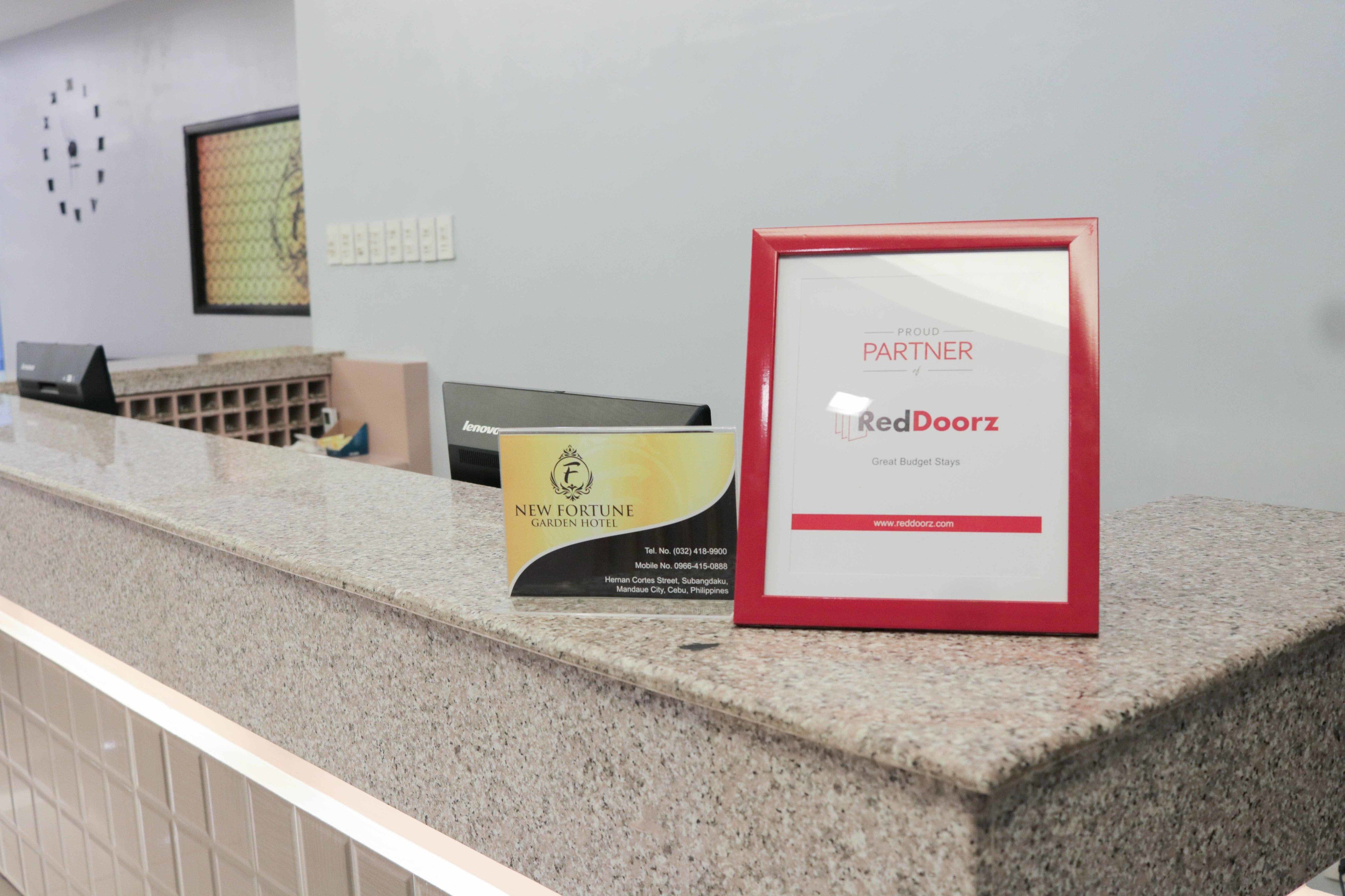 Un comptoir d’accueil orné d’un certificat encadré, d’une brochure du « New Fortune Garden Hotel » et d’un panneau « RedDoorz ».