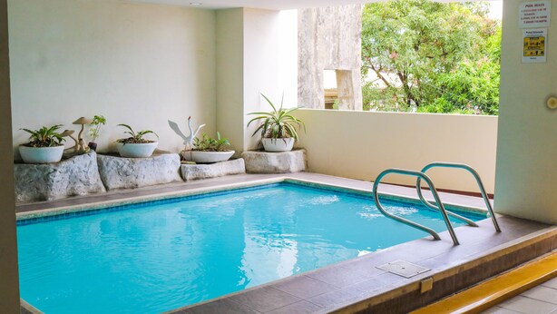 A swimming pool with a tiled edge, a metal ladder, and potted plants along the wall. - RedDoorz Plus @ Mabolo Cebu (Cebu City)