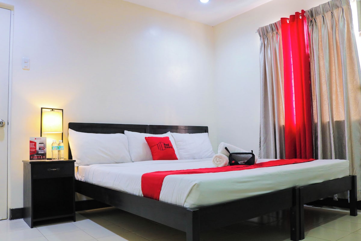 A neatly made bed with white and red bedding, a bedside table with a lamp, and a red curtain.
