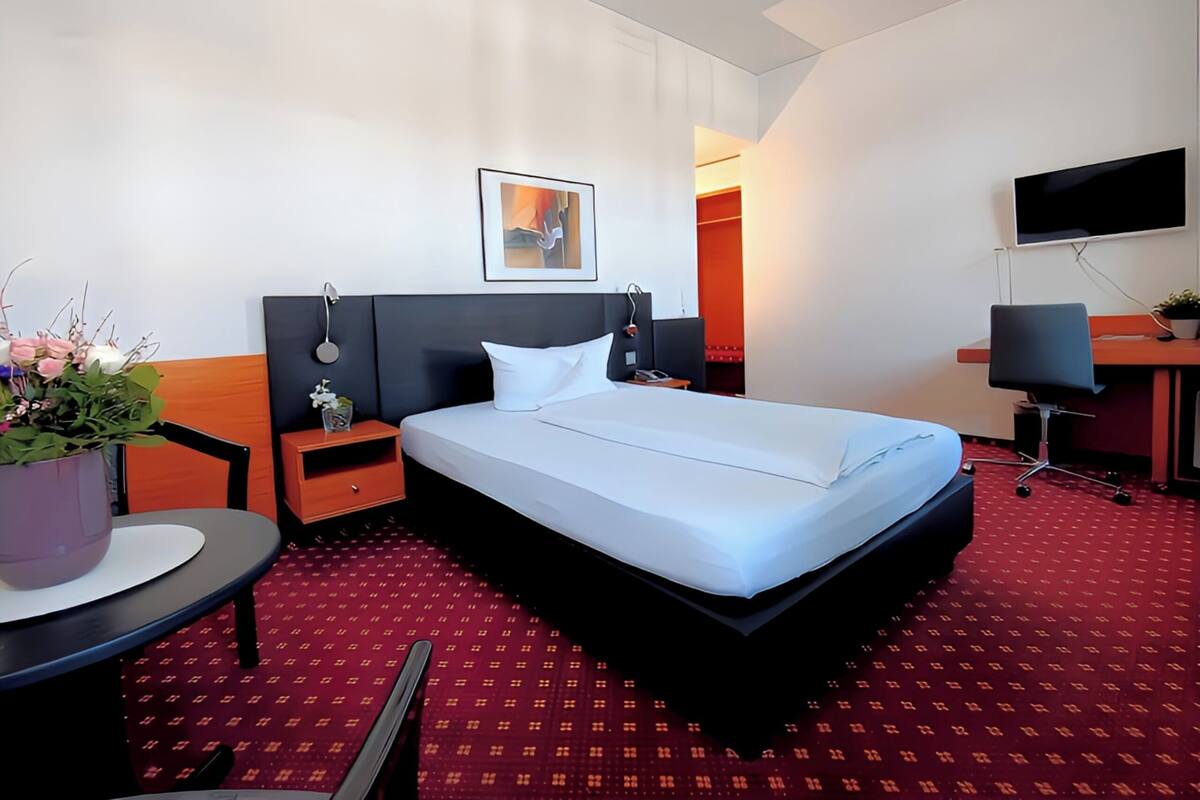 Una habitación de hotel con una cama grande, un escritorio, una silla, un televisor y una planta en maceta.