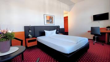 A hotel room with a large bed, a desk, a chair, a TV, and a potted plant.