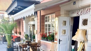 An outdoor seating area with wooden chairs and tables, a cobblestone path, and a building with a sign reading "SCHWERT Keller". - Hotel Schwert (Rastatt)