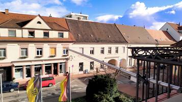 A street view with a building featuring a traditional European architectural style, a red car parked in front, and two flags on flagpoles.