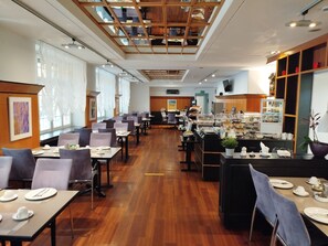 A spacious dining area with multiple tables and chairs, a buffet counter with various food items, and a ceiling with a wooden grid design. - Hotel Schwert (Rastatt)