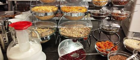 Ein Buffet mit verschiedenen Speisen in durchsichtigen Behältern, darunter Müsli, Nüsse und Trockenfrüchte.