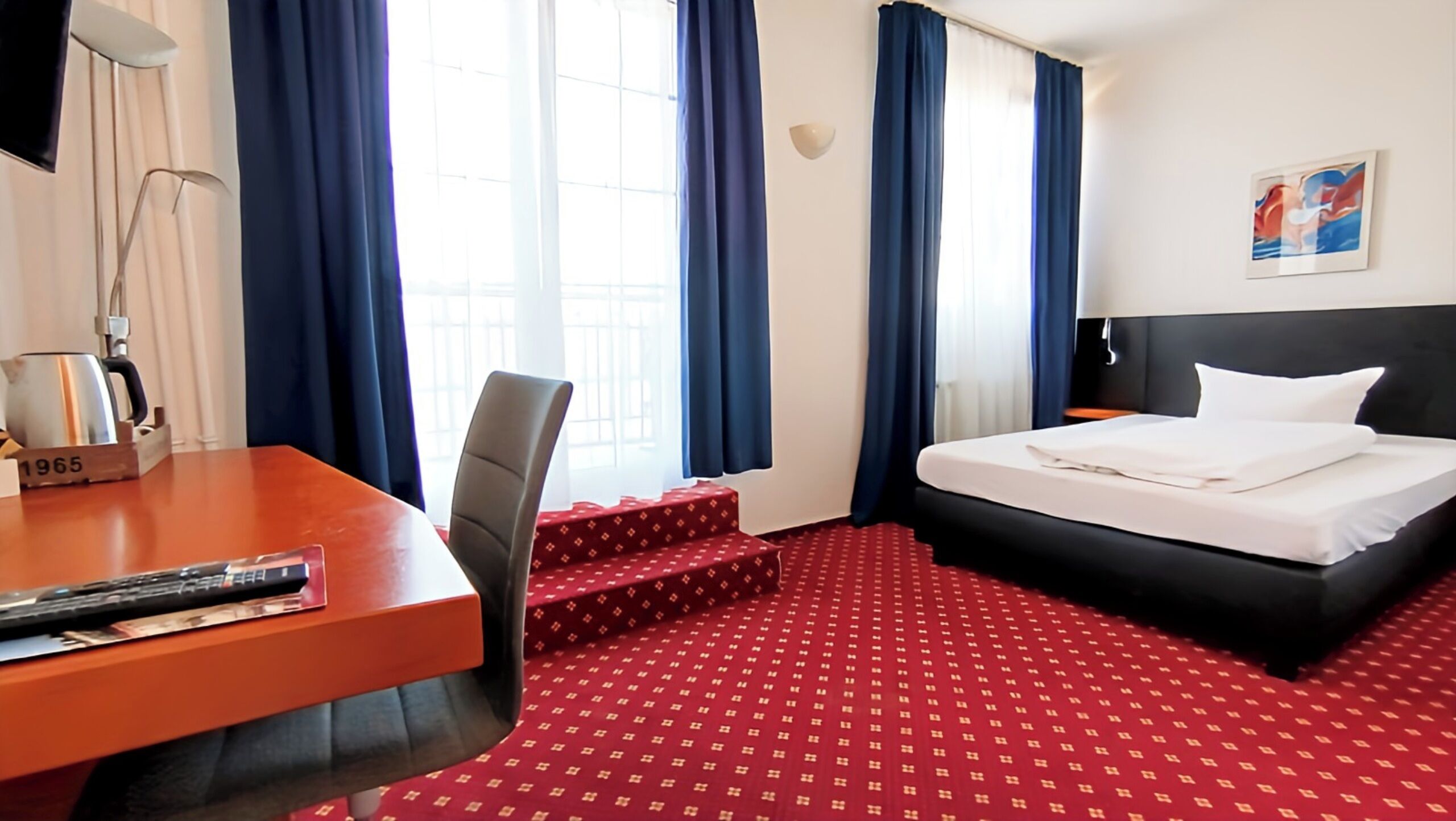 A hotel room with a bed, a desk, a chair, and a window with curtains.