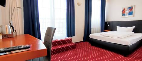 A hotel room with a bed, a desk, a chair, and a window with curtains.