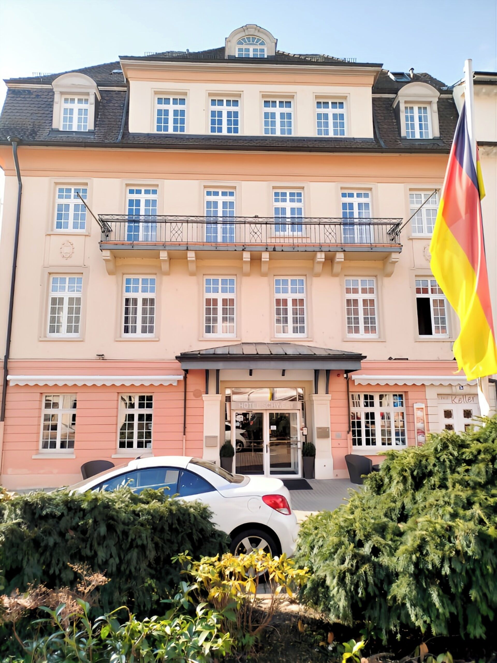 Un hotel con fachada simétrica, múltiples ventanas y una bandera.