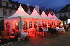 A tented outdoor dining area with tables and chairs, surrounded by buildings. - Hotel Schwert (Rastatt)