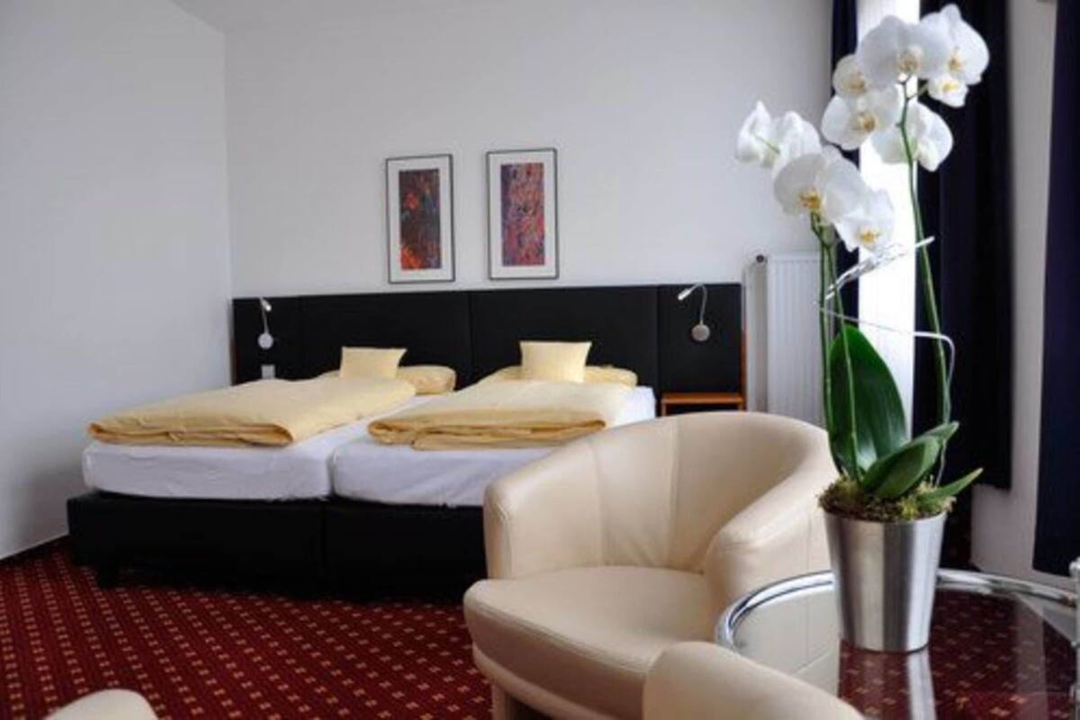 Habitación de hotel con dos camas, una silla, una mesita pequeña y una planta en maceta.