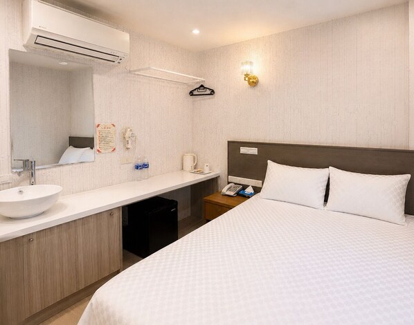 Habitación de hotel con cama, lavamanos, espejo, mesita de noche con teléfono y lámpara de pared.