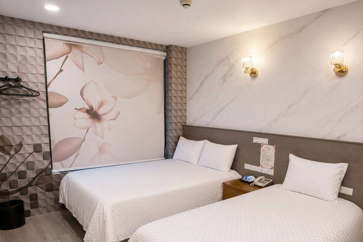 A hotel room with two beds, a bathroom, and a wall with a floral design.