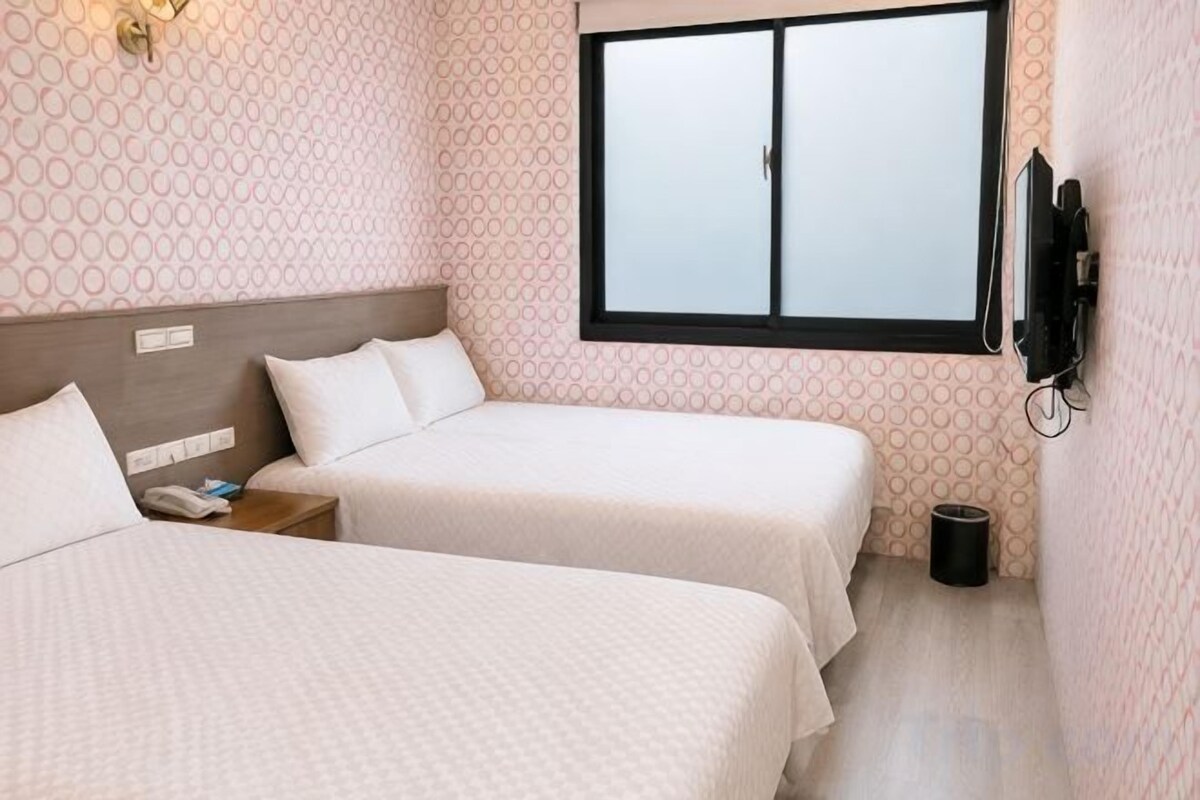 A hotel room with two beds, a television mounted on the wall, and a window.