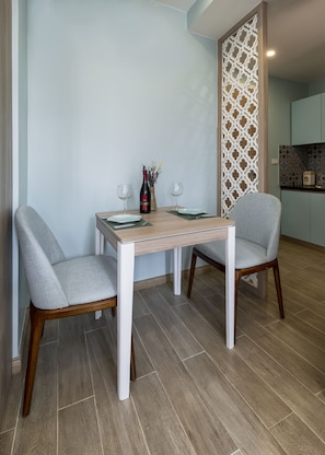 A dining area with a table set for two, two chairs, a bottle of wine, and a vase with flowers. - Soleil Apartment (Hanoi)