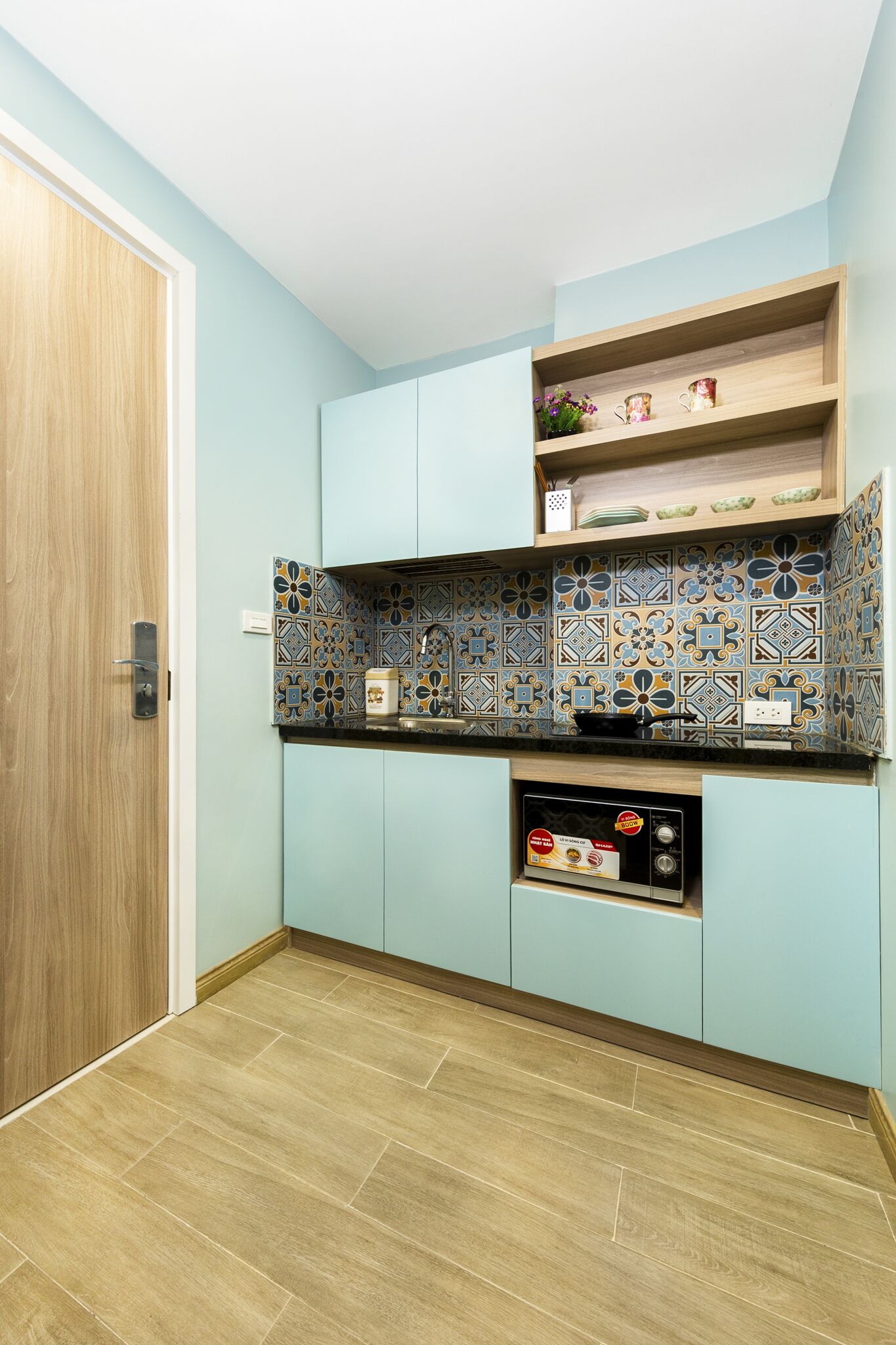A compact kitchen with light blue cabinets, a patterned backsplash, and a microwave.
