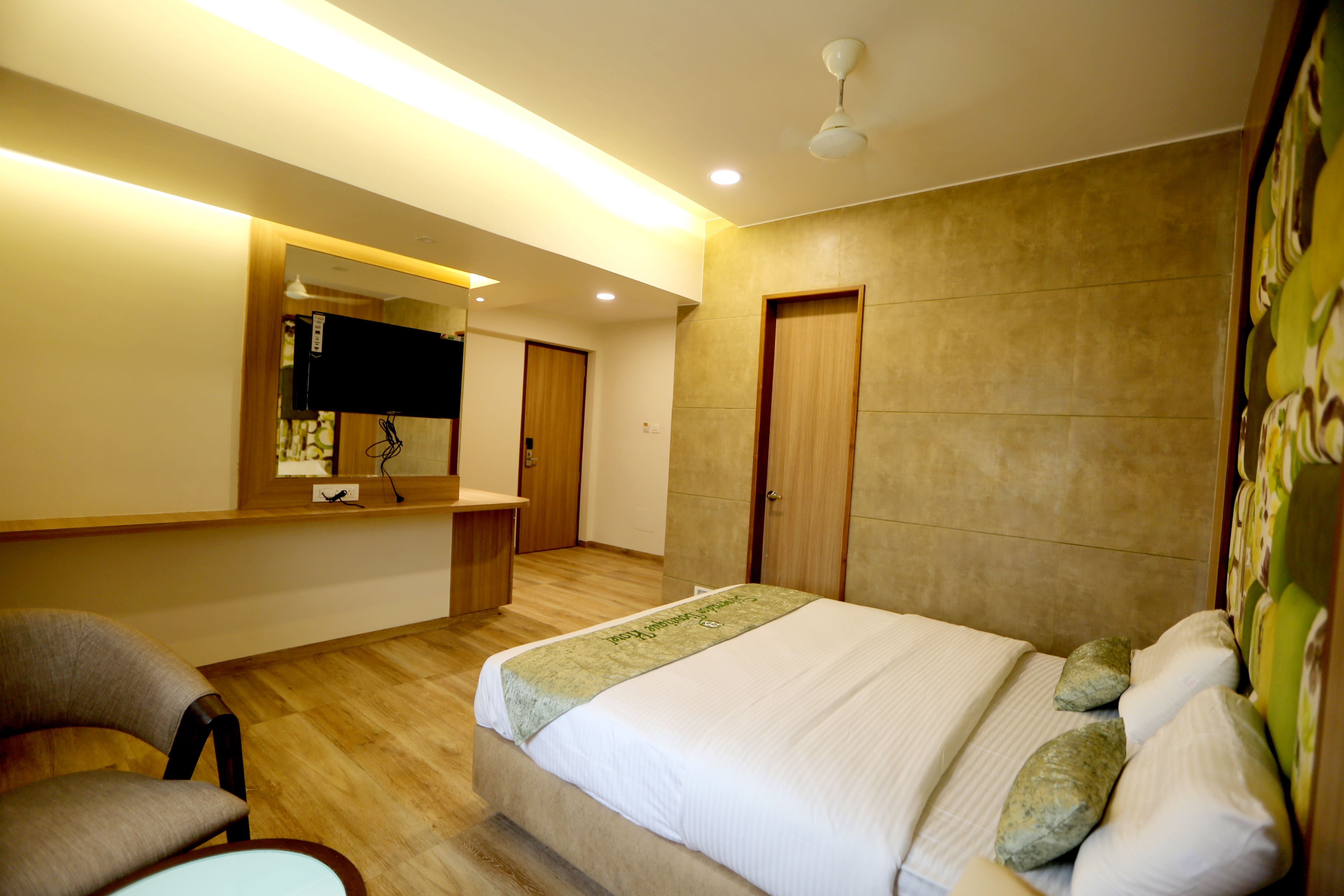 A hotel room with a bed, a chair, a desk, a mirror, and a door.