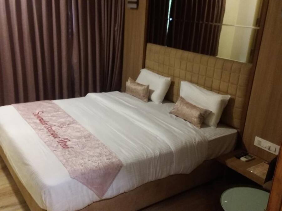 A hotel room with a large bed, a bedside table, a nightstand, and a window with curtains.