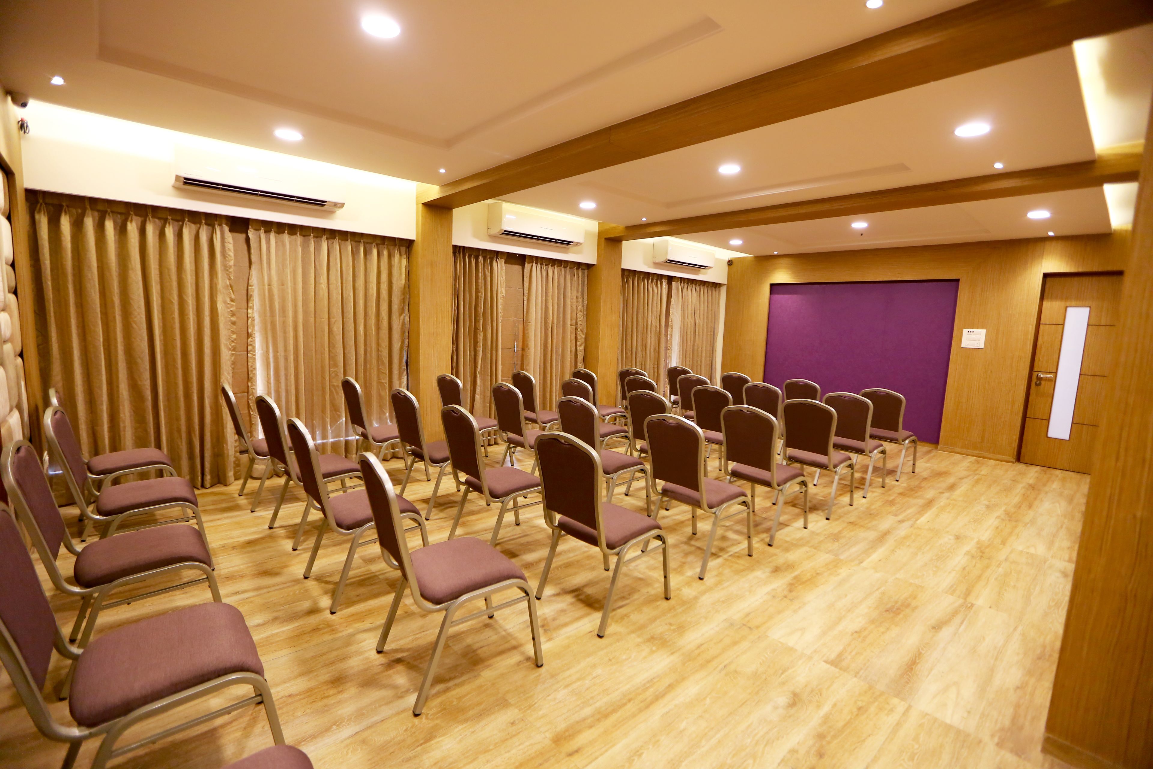 A conference room with rows of chairs, wooden floors, and air conditioning units.