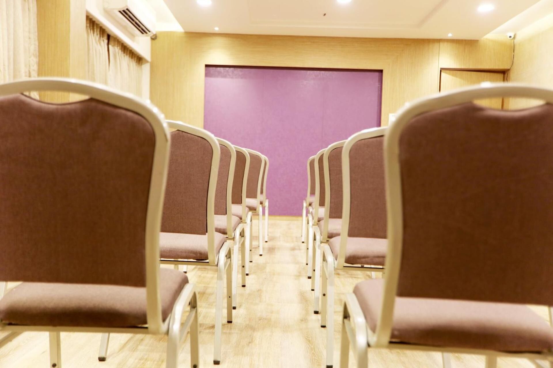 Rows of chairs facing a purple wall in a room with wooden flooring and a ceiling vent.